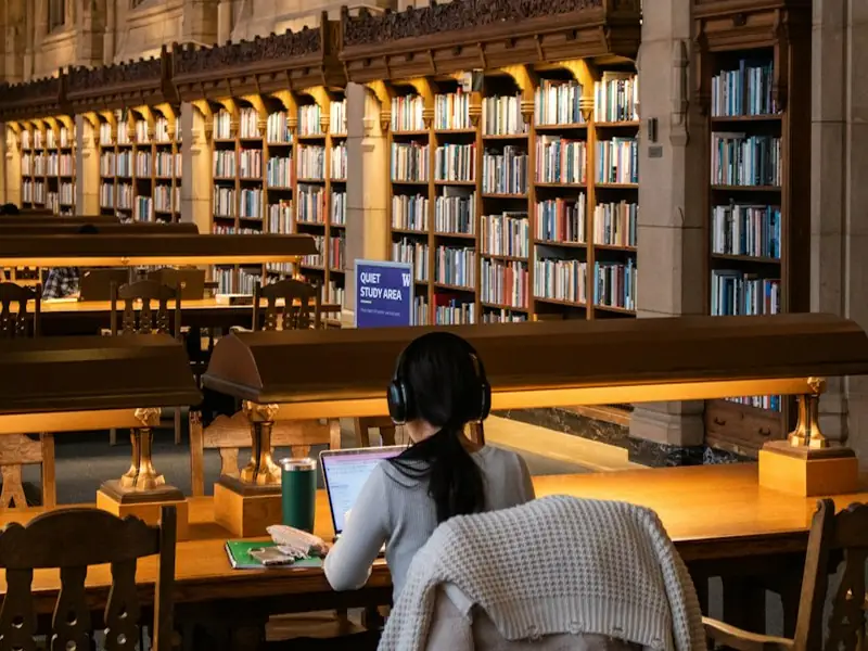 A student with headphones studying on a laptop in a library