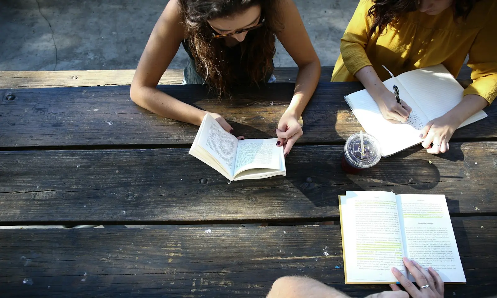 Two students reading and taking notes at an outdoor wooden table