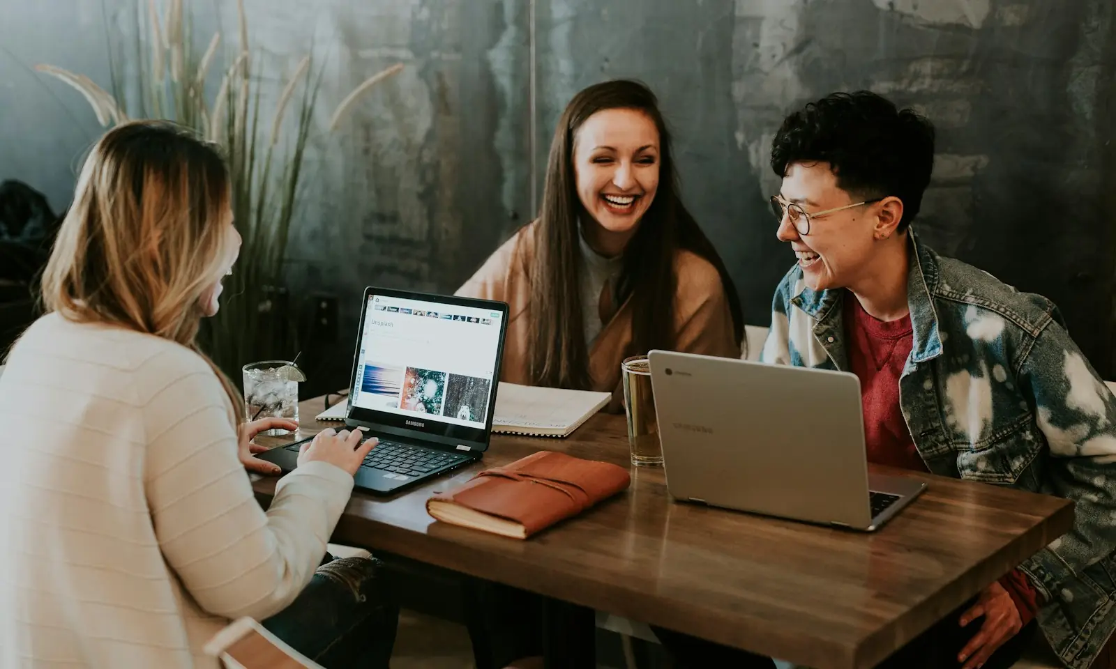 Three students laughing together around laptops at a table